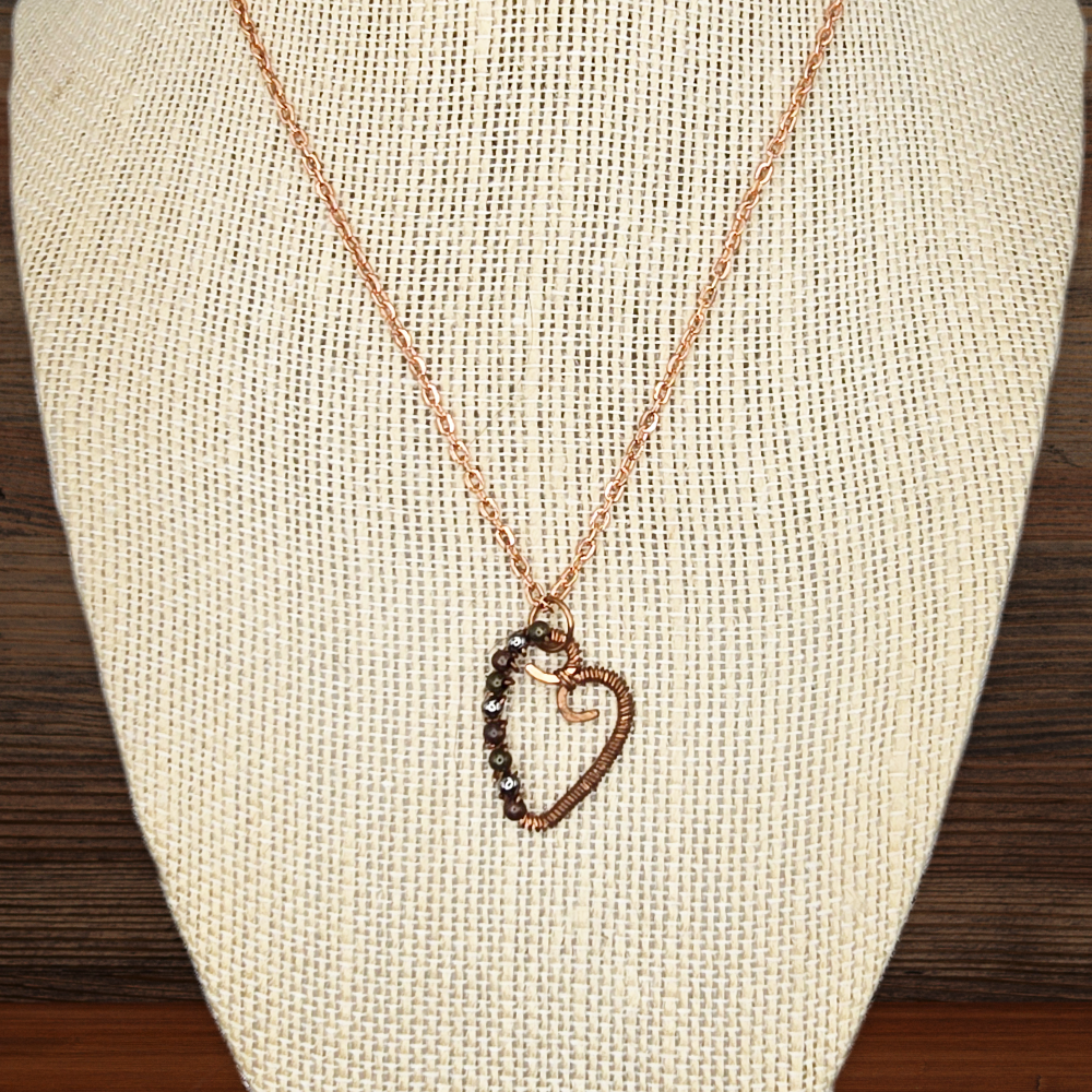 Necklace with a heart-shaped pendant on a beige fabric stand.