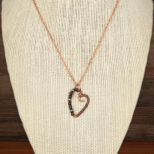 Necklace with a heart-shaped pendant on a beige fabric stand.